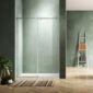 A modern bathroom with sage green textured walls, a glass sliding shower door, a striped rug on a wooden herringbone floor, a small potted plant, and a white ladder shelf holding folded towels.