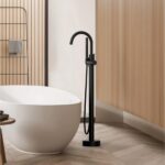 A modern bathroom with a white freestanding tub, the Halo Floor Mount Tub Filler With Hand Shower in black, light wood panel walls, and a geometric tile floor.