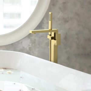 The Quadra Floor Mount Tub Filler With Hand Shower, featuring a modern square gold design, is installed beside a white bathtub filled with water and flower petals, set against a textured gray wall and round window.