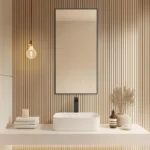 Minimalist bathroom features Metal Framed Mirrors, a square white sink, stacked towels, dried plants in a vase, soap, candle, and a hanging exposed bulb light against vertical wooden slat wall panels.