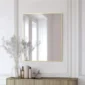 A modern Metal Framed Mirror with a thin gold edge hangs on a white paneled wall above a beige console table holding glass vases with dried flowers, bottles, and a small decorative bird statue.