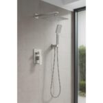 The Quadra Pressure Balanced Wall Mount Shower System features a large square overhead showerhead, a handheld attachment, and brushed metal controls, installed against light gray tiles beside a glass window.
