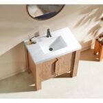 The Munich 36 Inch Bathroom Vanity with Top features a white rectangular sink, black faucet, and light wood cabinet beneath a round mirror on a beige wall. Sunlight streams in, casting elegant shadows on the floor and wall.
