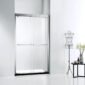 A modern bathroom features an ASD Cascade Shower Door – Bypass Sliding framed in silver, a black metal dress form, and a small table with a vase of flowers against a white wall.