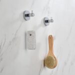 Two Halo Robe Hooks in chrome finish are mounted on a marble wall, each holding a pumice stone on a string and a wooden bath brush with bristle head.
