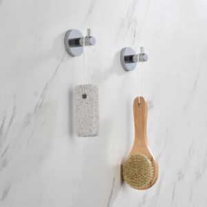 Two Halo Robe Hooks in chrome finish are mounted on a marble wall, each holding a pumice stone on a string and a wooden bath brush with bristle head.