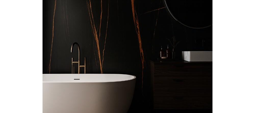 Minimalist bathroom with a white freestanding bathtub, matte black faucet, and large format tiles featuring bold orange veining on black walls and floor. Includes a dark vanity, round mirror, and soft, dramatic lighting.