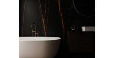 Minimalist bathroom with a white freestanding bathtub, matte black faucet, and large format tiles featuring bold orange veining on black walls and floor. Includes a dark vanity, round mirror, and soft, dramatic lighting.