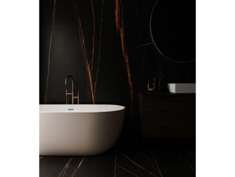 Minimalist bathroom with a white freestanding bathtub, matte black faucet, and large format tiles featuring bold orange veining on black walls and floor. Includes a dark vanity, round mirror, and soft, dramatic lighting.