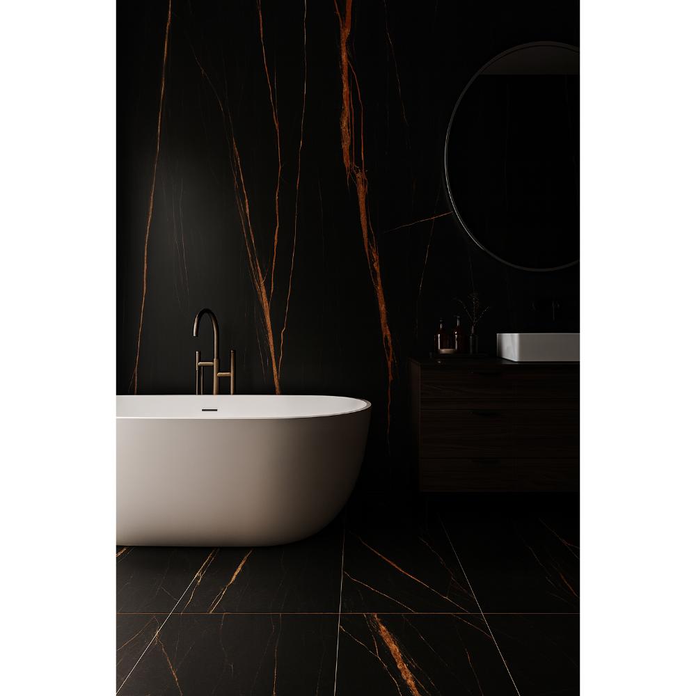 Minimalist bathroom with a white freestanding bathtub, matte black faucet, and large format tiles featuring bold orange veining on black walls and floor. Includes a dark vanity, round mirror, and soft, dramatic lighting.