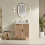 Minimalist bathroom featuring a Liora 36 Inch Bathroom Vanity with white countertop, oval mirror, gold fixtures, twin wall sconces, a potted plant, and a small wooden stool with books—all set against a beige wall.