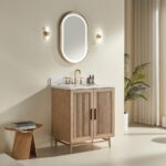 A light wood Liora 36 Inch Bathroom Vanity with a white countertop, gold faucet, and bottles sits below an oval gold-framed mirror. Modern decor is completed by wall sconces, a plant, beige walls, curtains, and a small stool with books.