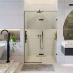 A modern bathroom featuring the Nova Hinged Frameless Shower Door with black fixtures, a freestanding bathtub, wall-mounted faucet, gray bath mat, round mirror, and plants for a touch of greenery.