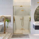 A modern bathroom featuring the Nova Hinged Frameless Shower Door, gold fixtures, a freestanding bathtub, a terrazzo sink, a round mirror, green plants, and light-colored tiles.