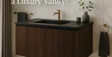 A modern bathroom with a floating dark wood luxury vanity, black countertop, gold faucet, round mirror, and minimal decor. Text on image reads, What Makes a Luxury Vanity?.