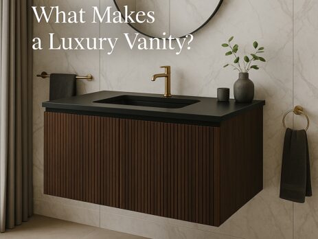 A modern bathroom with a floating dark wood luxury vanity, black countertop, gold faucet, round mirror, and minimal decor. Text on image reads, What Makes a Luxury Vanity?.