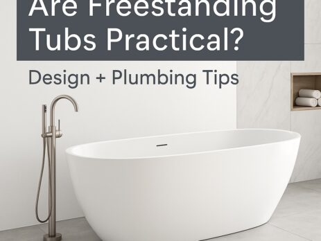 A modern bathroom with a white freestanding bathtub, floor-mounted faucet, and built-in shelf. Text reads: Are Freestanding Tubs Practical? Design + Plumbing Tips.