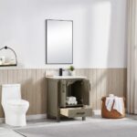A modern bathroom features the Basel 24 Inch Bathroom Vanity with its door and drawer open to reveal towels inside, complemented by a large wall mirror, a basket of towels, wood paneling, neutral decor, and a gray rug.