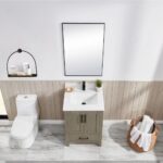 A modern bathroom features a white toilet, the Basel 24 Inch Bathroom Vanity in green with a white sink, a rectangular mirror above, a wall shelf for toiletries, and a wicker basket holding towels on a marble floor.