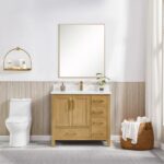 A modern bathroom showcases the Basel 36 Inch Bathroom Vanity with a white countertop and rectangular mirror above. A toilet and gold shelf with toiletries are to the left, while a towel-filled basket sits near a sunlit window on the right.