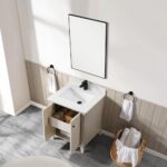 A modern bathroom with the Torino 24 Inch Bathroom Vanity Cabinet, featuring a white countertop, black faucet, open drawer and cabinet, rectangular mirror above, two towel rings with white towels, and a basket of rolled towels on tile flooring.