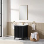A modern bathroom features the Torino 24 Inch Bathroom Vanity Cabinet in black with gold fixtures, a rectangular gold-framed mirror, two towels on gold rings, and a woven basket with extra towels on a tiled floor.