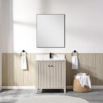 A minimalist bathroom features a rectangular mirror above the Torino 30 Inch Bathroom Vanity Cabinet in light wood, flanked by towel rings with white towels. A wicker basket with rolled towels sits on the tiled floor beside the vanity.