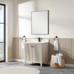 A bathroom with the Torino 30 Inch Bathroom Vanity Cabinet, topped by a framed mirror and black faucet. Towel rings flank the vanity, while a basket of rolled white towels sits beside it. Natural light pours in from a large window.