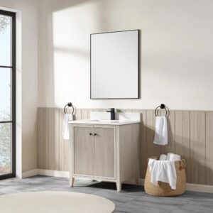 A bathroom with the Torino 30 Inch Bathroom Vanity Cabinet, topped by a framed mirror and black faucet. Towel rings flank the vanity, while a basket of rolled white towels sits beside it. Natural light pours in from a large window.