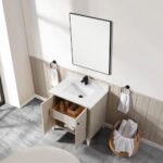 The Torino 30 Inch Bathroom Vanity Cabinet features an open drawer and cabinet, white countertop and sink, black faucet, rectangular mirror above, towel rings with white towels on each side, and a basket with rolled towels on a gray marble floor.