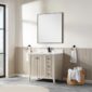 A modern bathroom features the Torino 36 Inch Bathroom Vanity Cabinet with drawers, black faucet, square mirror, towel rings with white towels, and a woven basket on a gray tile floor. Sunlight streams in from a large window.