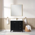 A modern bathroom showcases the Torino 36 Inch Bathroom Vanity Cabinet with drawers, a square gold-framed mirror above, a white sink, gold-accented hardware, two towel rings with white towels, and a wicker basket of rolled towels on the floor.