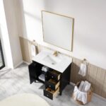 A modern bathroom features the Torino 36 Inch Bathroom Vanity Cabinet with drawers, a white countertop, black finish, and gold faucet. The open cabinet displays towels and toiletries. Nearby are a large mirror, towel rings, and a basket with rolled towels.
