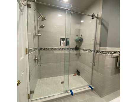 Modern bathroom with a large glass-enclosed shower, white subway tile walls, a decorative tile border, silver fixtures, a built-in shelf, and gray tile flooring. Blue painter’s tape is on the shower door.